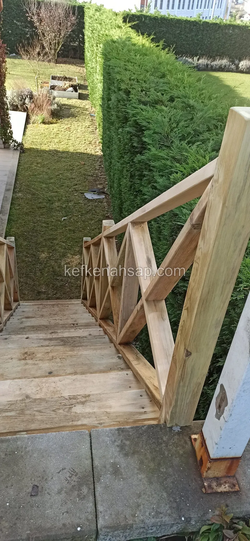 Canlı çitle çevrili bahçeye inen ahşap basamakların yanında çapraz desenli ahşap korkuluk