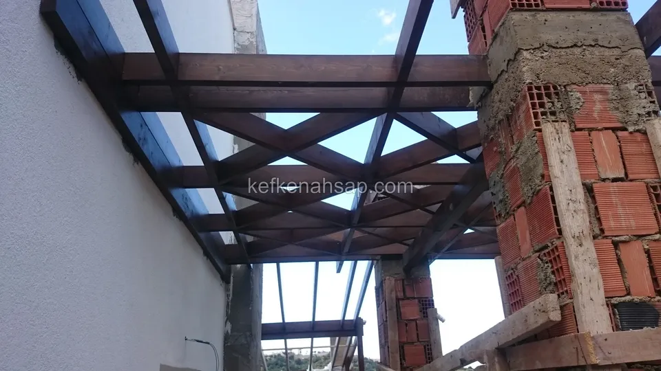 Çapraz oturan kirişlerden oluşan pergola köşesi, yanında harcı görünen tuğla kolonlar ve beyaz duvar