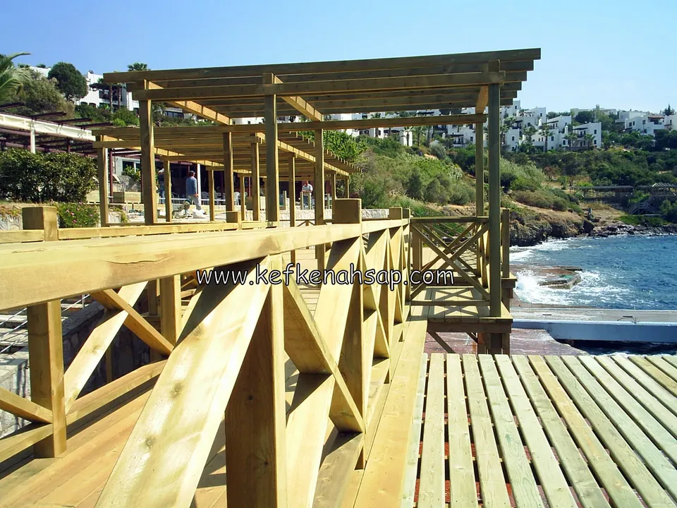 Deniz kıyısında çapraz çıtalı korkuluğu olan ahşap platform ve üzerinde yükselen pergola iskeleti