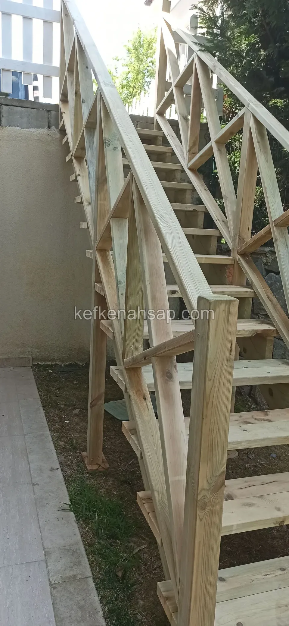 Çaprazlı korkuluk detaylı ahşap merdiven; yanında duvar ve beyaz çit