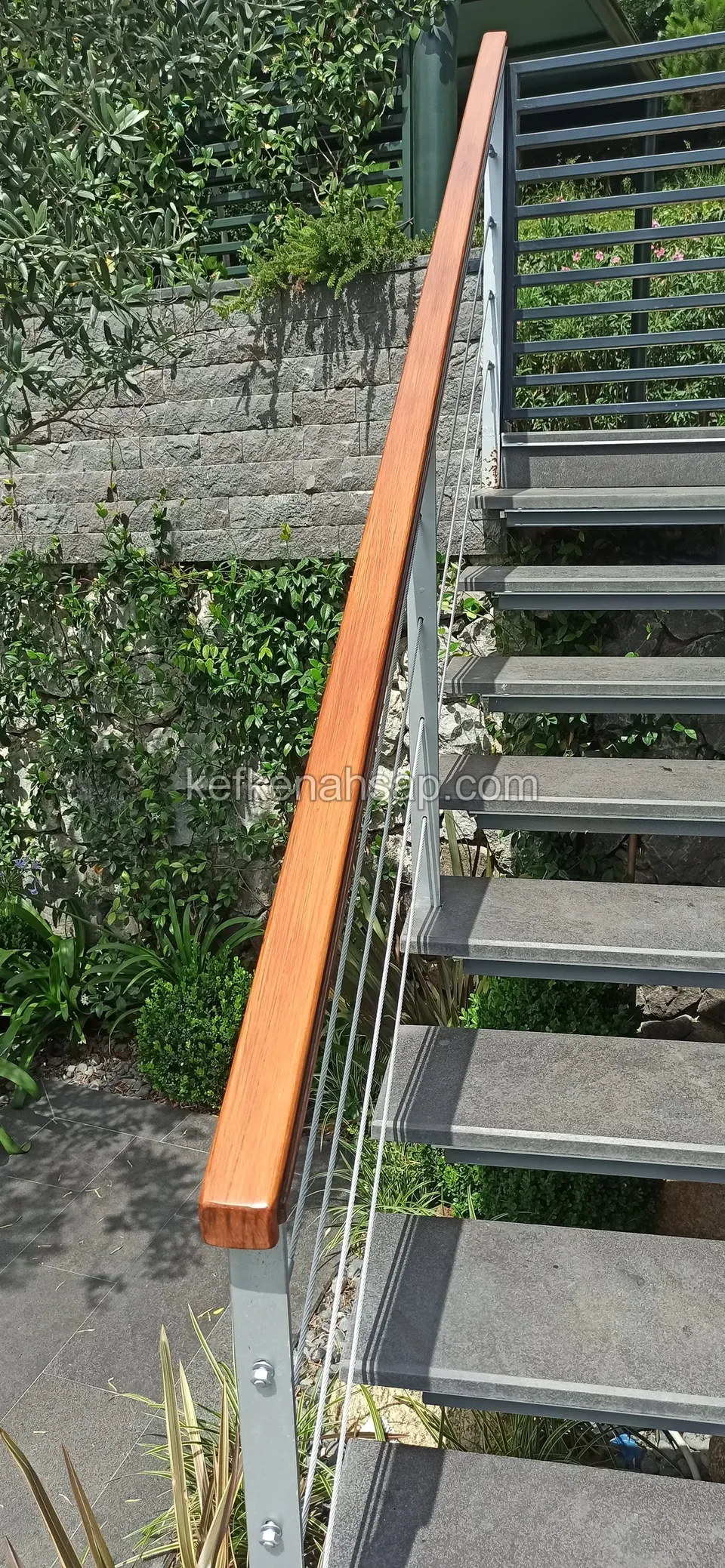 Horizontal steel cables and a varnished timber handrail beside an outdoor staircase with grey treads