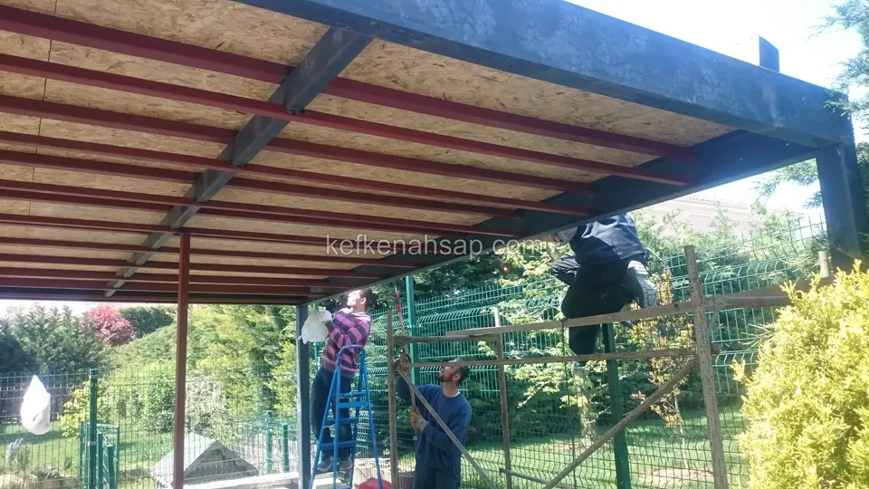 Çelik taşıyıcılar üzerine döşenmiş OSB kaplı çatı, altında merdiven başında çalışan iki kişi, arkada bahçe