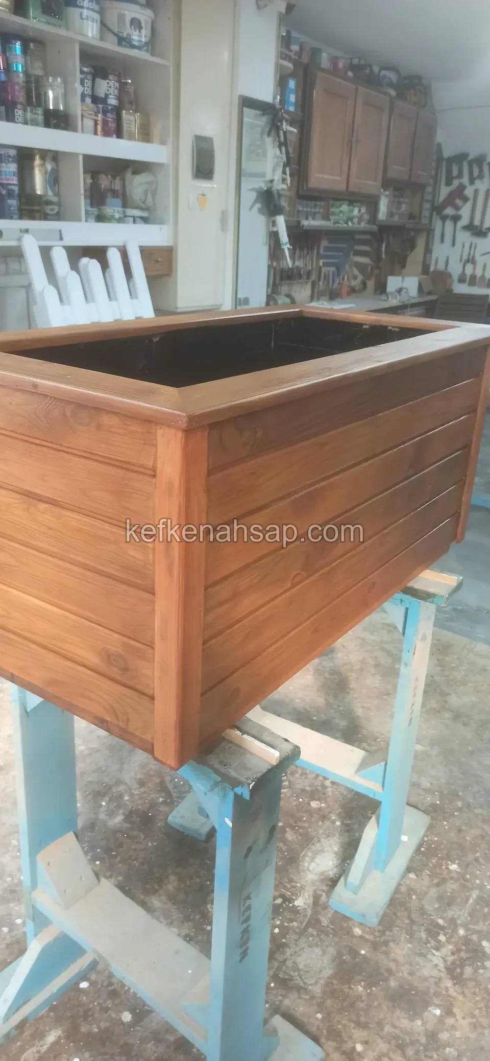 Varnished timber planter on a steel stand with workshop shelves and cupboards behind