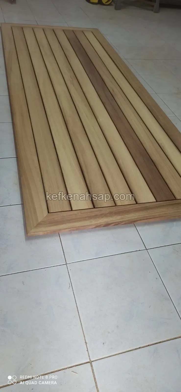 Seramik zemin üzerinde duran, gönye köşe çerçeveli ve paralel latalı ahşap deck paneli.