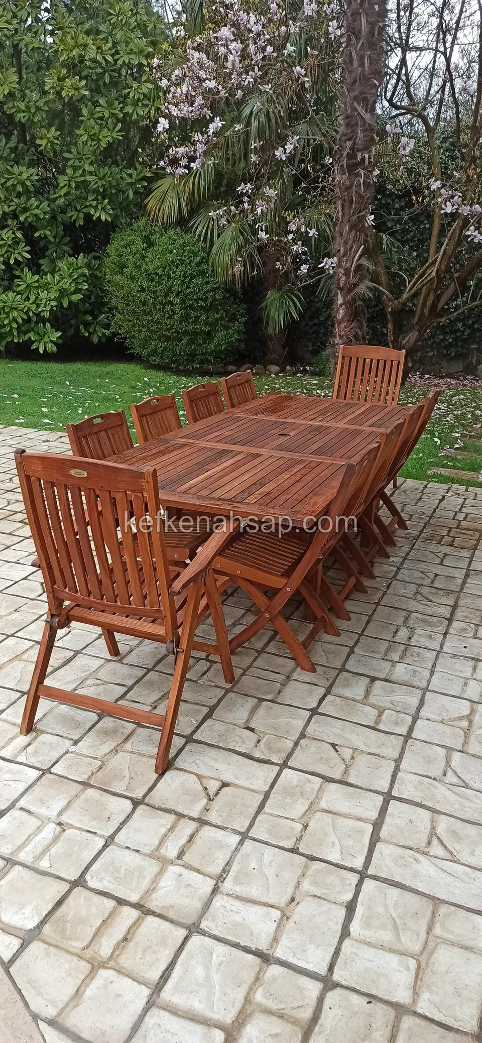 In einem Garten mit Magnolie und Sträuchern ein sehr langer Holztisch mit Klappstühlen an beiden Seiten