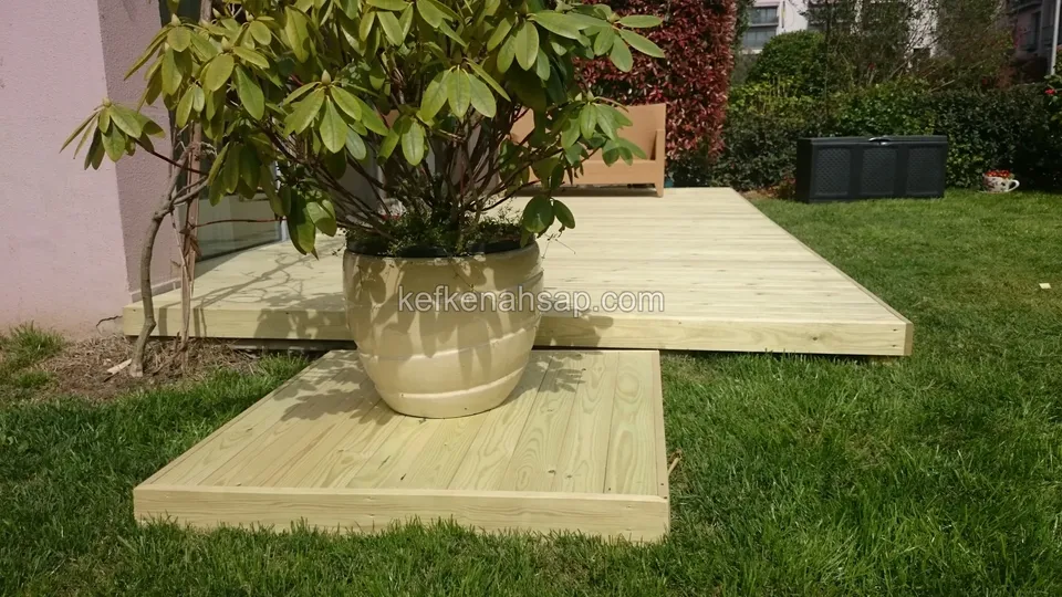 Çimenlik üzerinde iki parça halinde açık renkli deck, üzerinde büyük bir saksı bitki