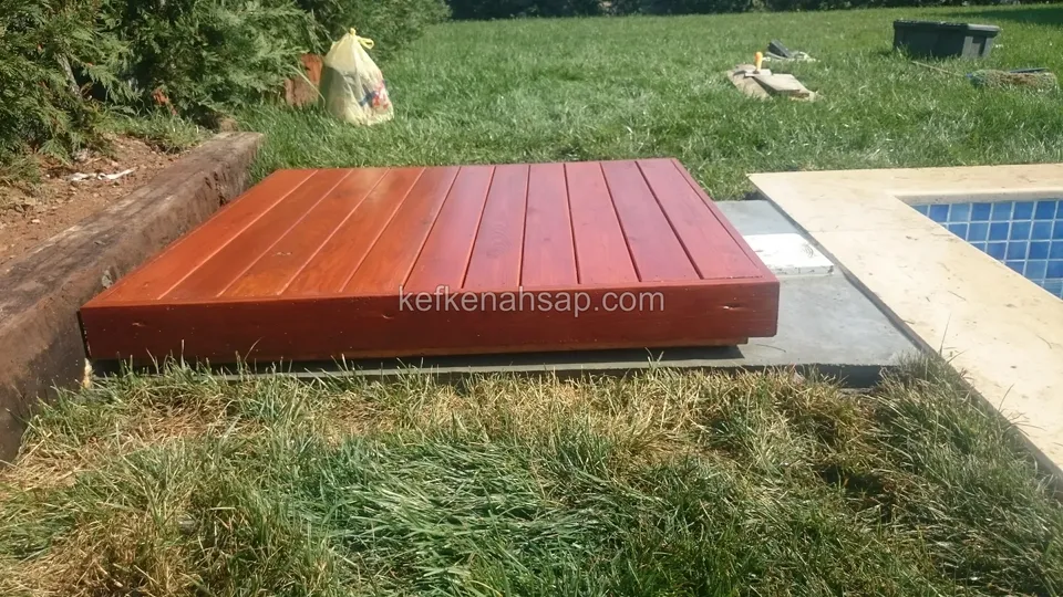 Red-brown timber deck platform near a pool, sitting on lawn and stone paving