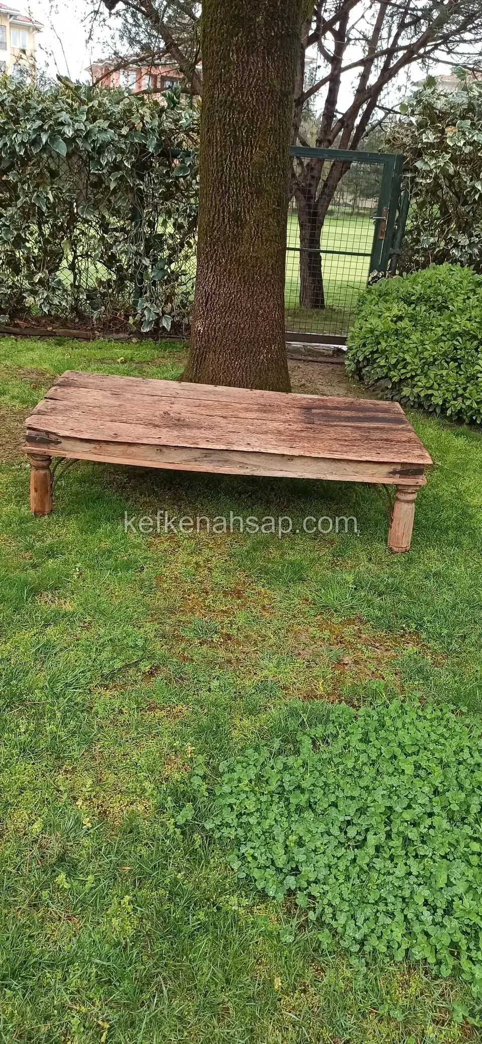 A low dark timber table with short legs and an aged look on a garden lawn beside a thick tree trunk