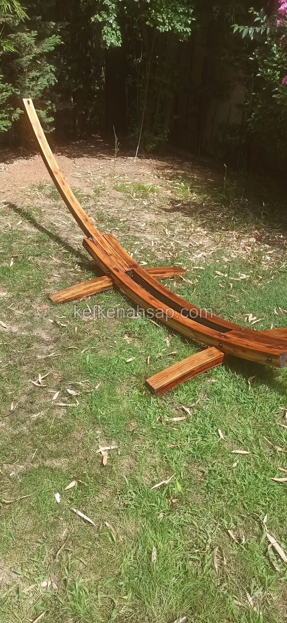 A curved orange-brown timber hammock stand with both ends on the ground in a lawn garden
