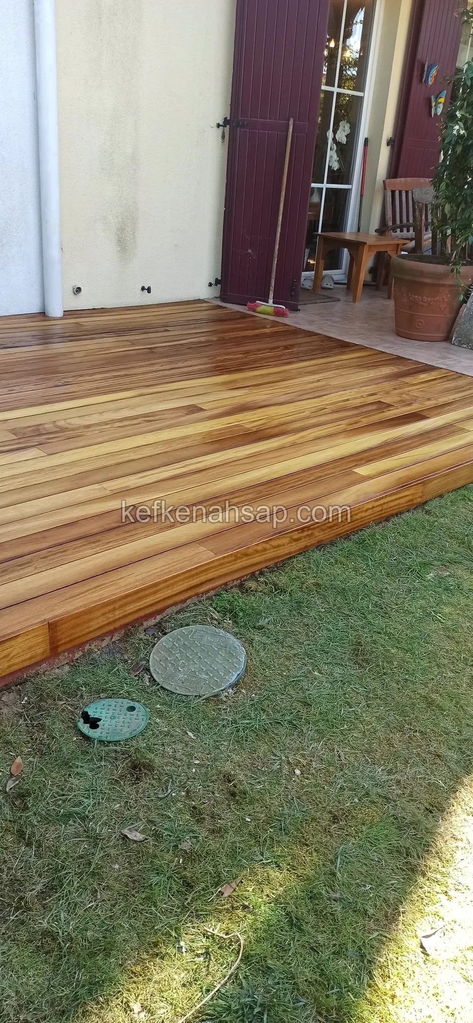 Glossy multi-tone deck in front of a glass door with burgundy shutters, ending at the edge of the lawn