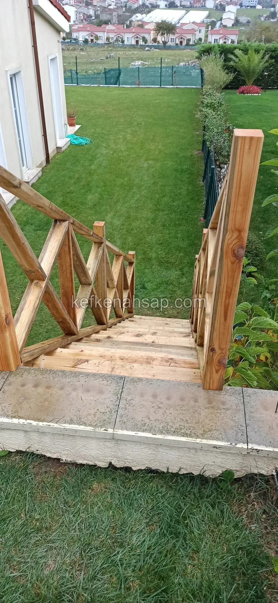 Holztreppe mit Diagonalgeländer von einer Betonmauer hinab auf den Rasen, von oben gesehen