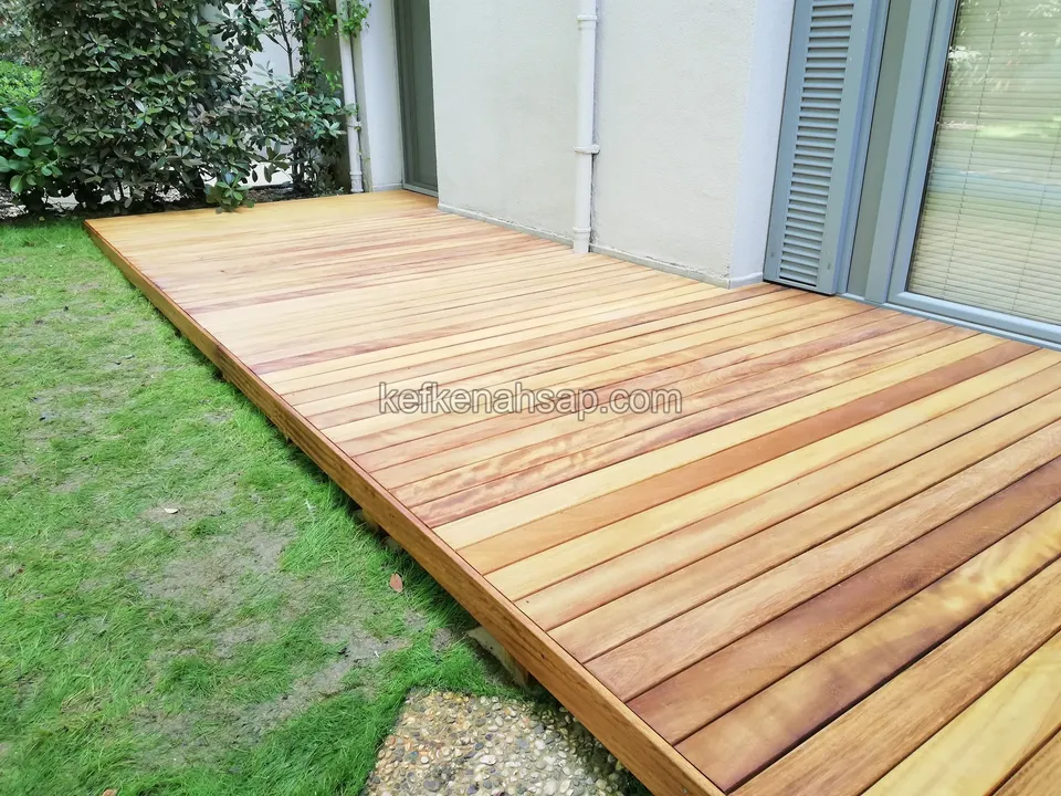 Wide, glossy, red-toned timber deck running beside a lawn, seen in perspective