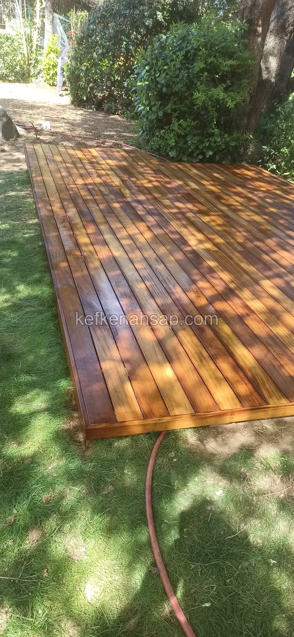 Glänzendes orangebraunes Deck auf dem Rasen, daneben ein sich windender roter Schlauch