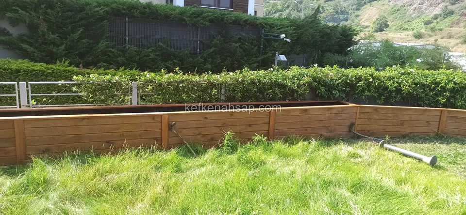 Long, low varnished timber planter built at the edge of the lawn in front of shrubs
