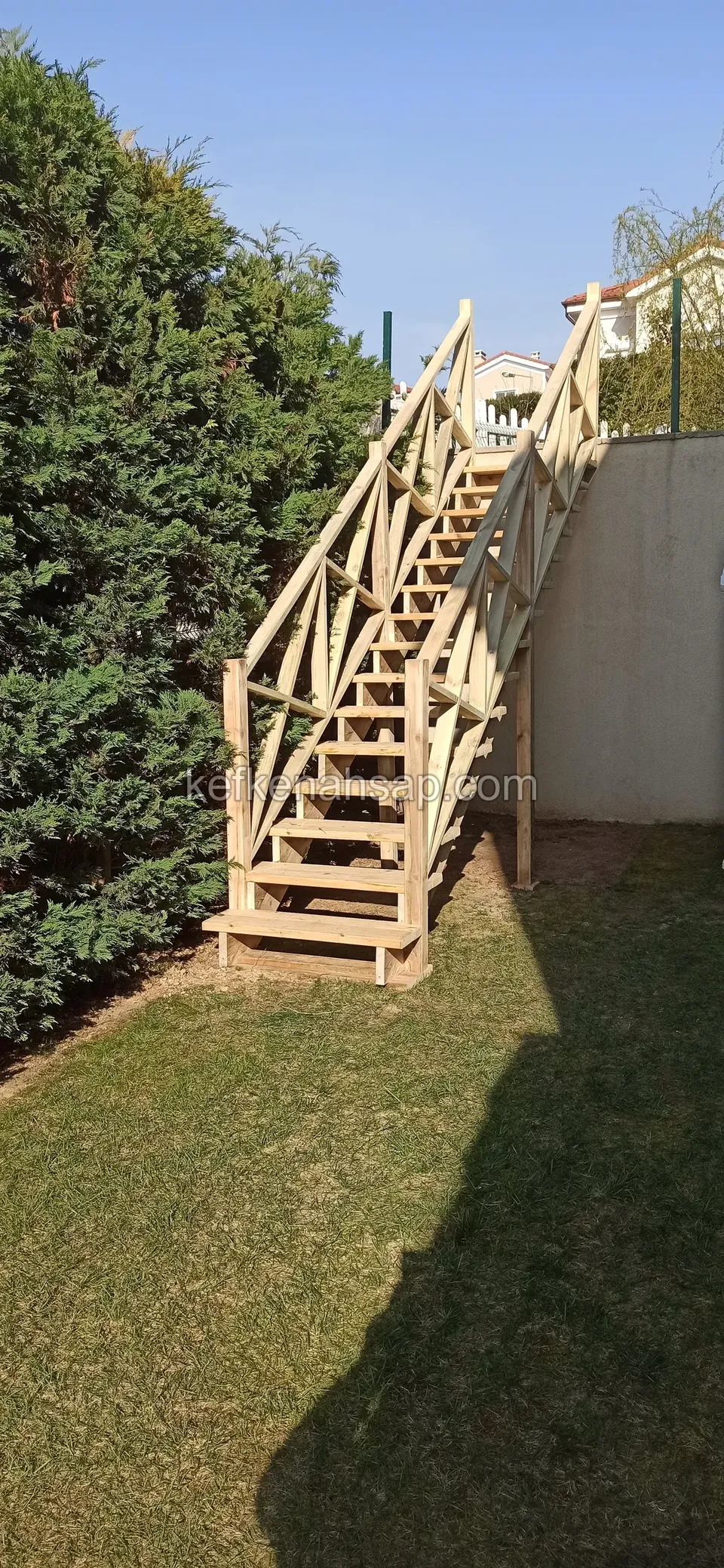 Holztreppe neben einer hohen grünen Hecke, die vom Rasen auf die Gartenmauer führt