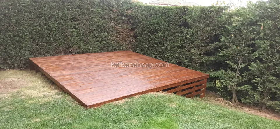 Wide dark-toned timber deck set on the lawn in a garden corner enclosed by tall hedges