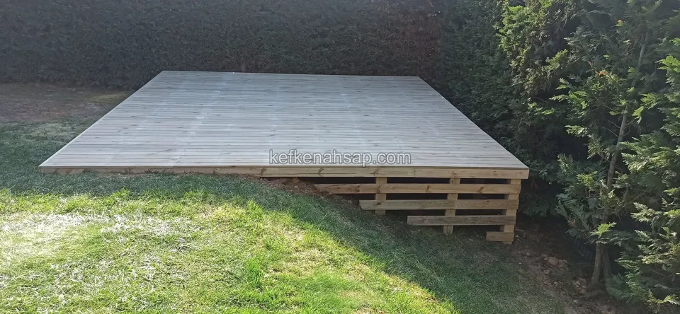 Pale rectangular deck raised on pallet-like timber supports in front of a hedge