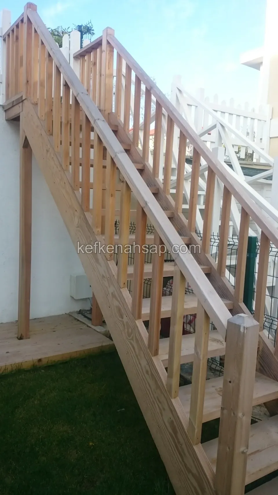 Çıtalı ahşap korkuluklu uzun ahşap merdiven; altta çimlik, üstte beyaz çıtalı çit