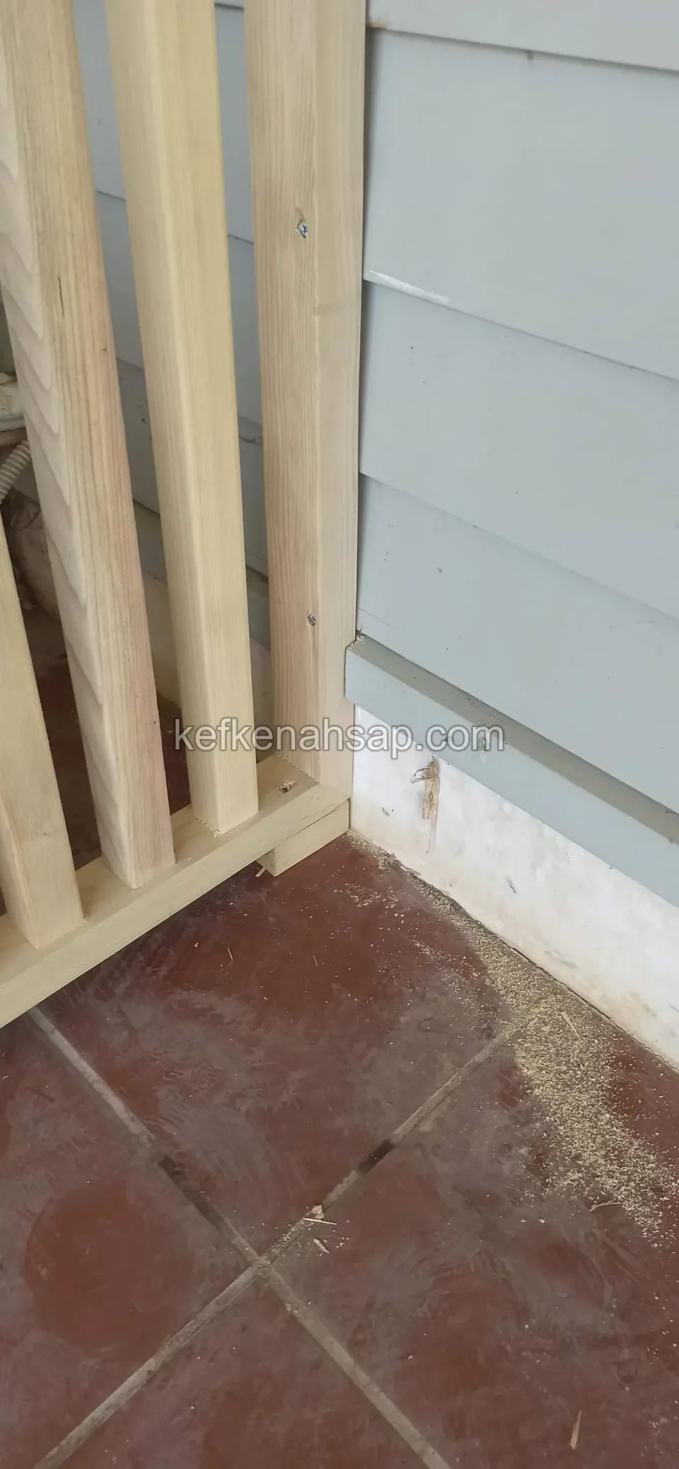 Kırmızı karo zemin üzerinde duran açık tonlu çıtalı panelin köşesi, yanında gri cephe kaplaması
