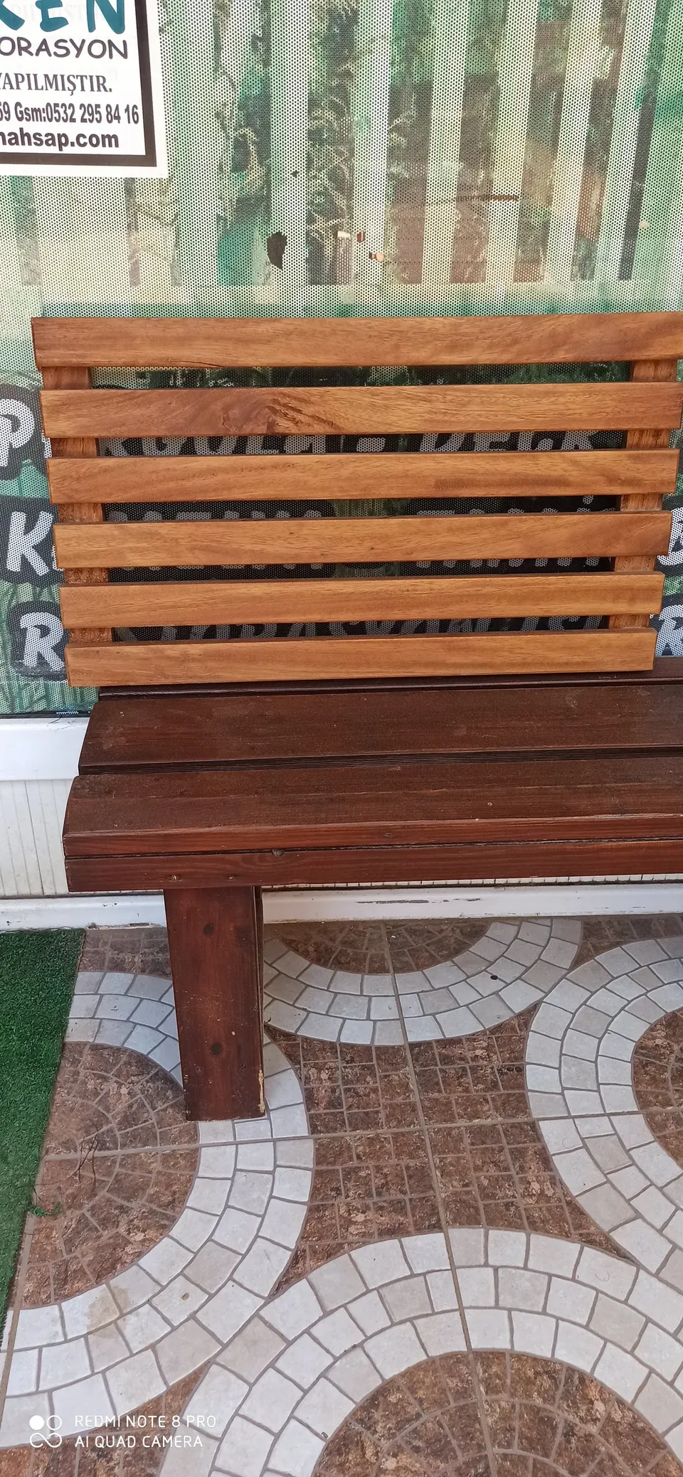 Eine Holzbank mit hellem Rücken aus waagerechten Latten und dunkel lackierter Sitzfläche samt Beinen auf Mosaikboden