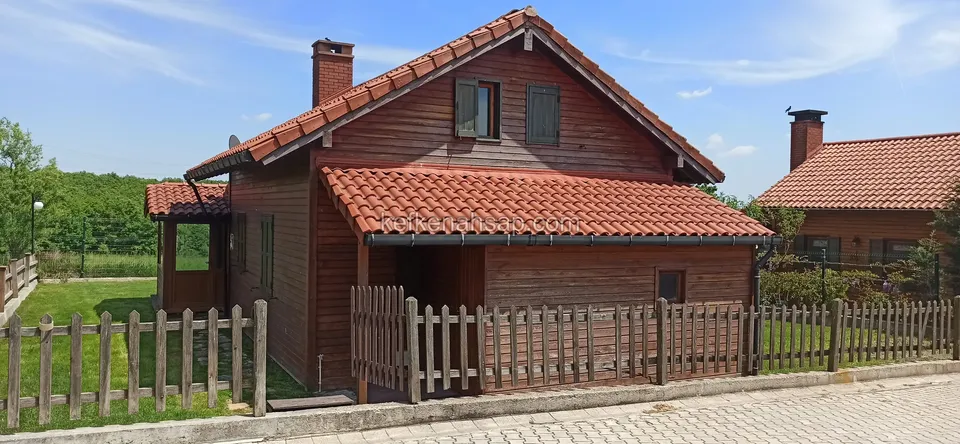 Kiremit çatılı, bacalı, kızıl kahve tonlu ahşap ev ve önündeki ahşap bahçe çiti