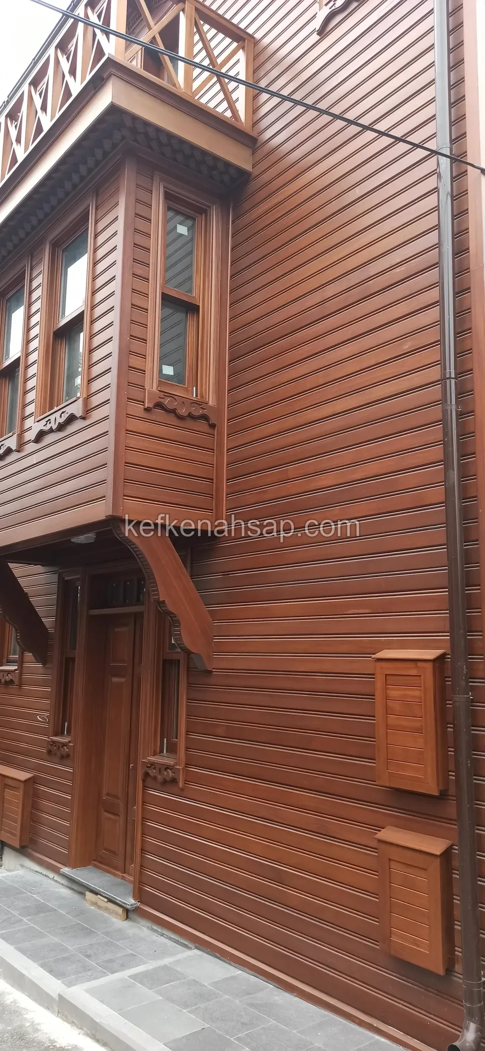Yatay ahşap kaplamalı kızıl kahve tonlu dar cephe, üst katta cumba ve altta ahşap kapı