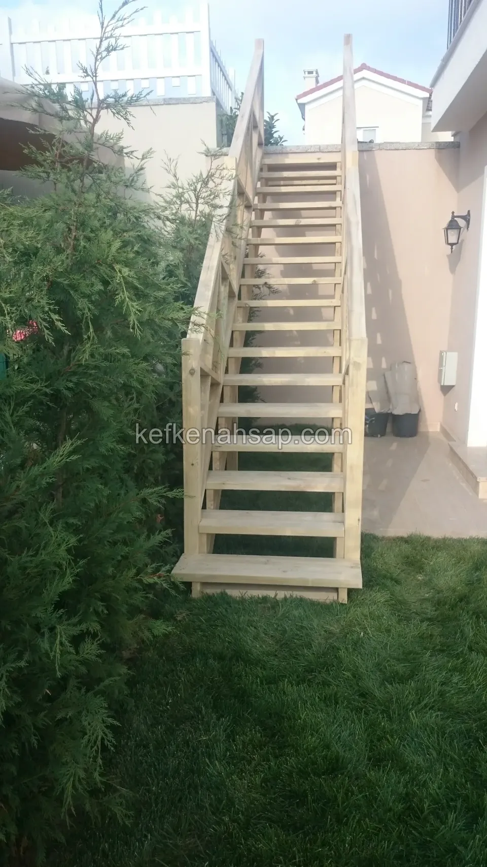 Holzaußentreppe zwischen Hauswand und Sträuchern in einem schmalen Gartengang, aus der Ferne gesehen