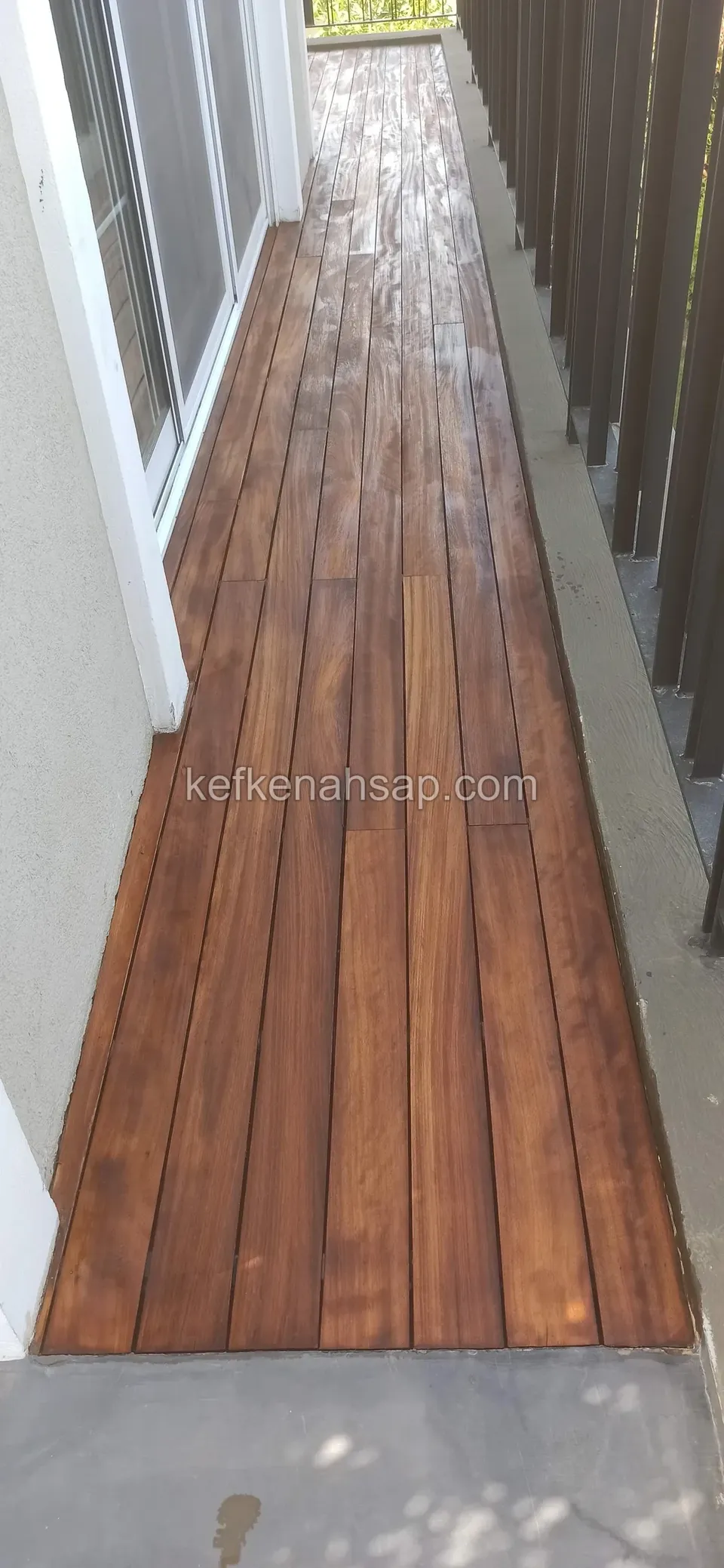 Red-brown polished deck laid lengthwise along a narrow balcony beside a glass door