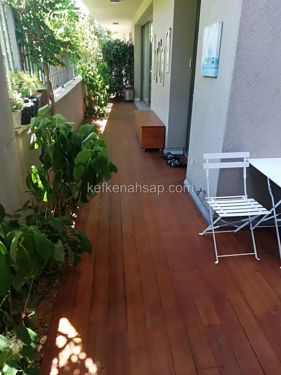 Reddish-brown timber deck on a narrow balcony with a white folding chair and plants