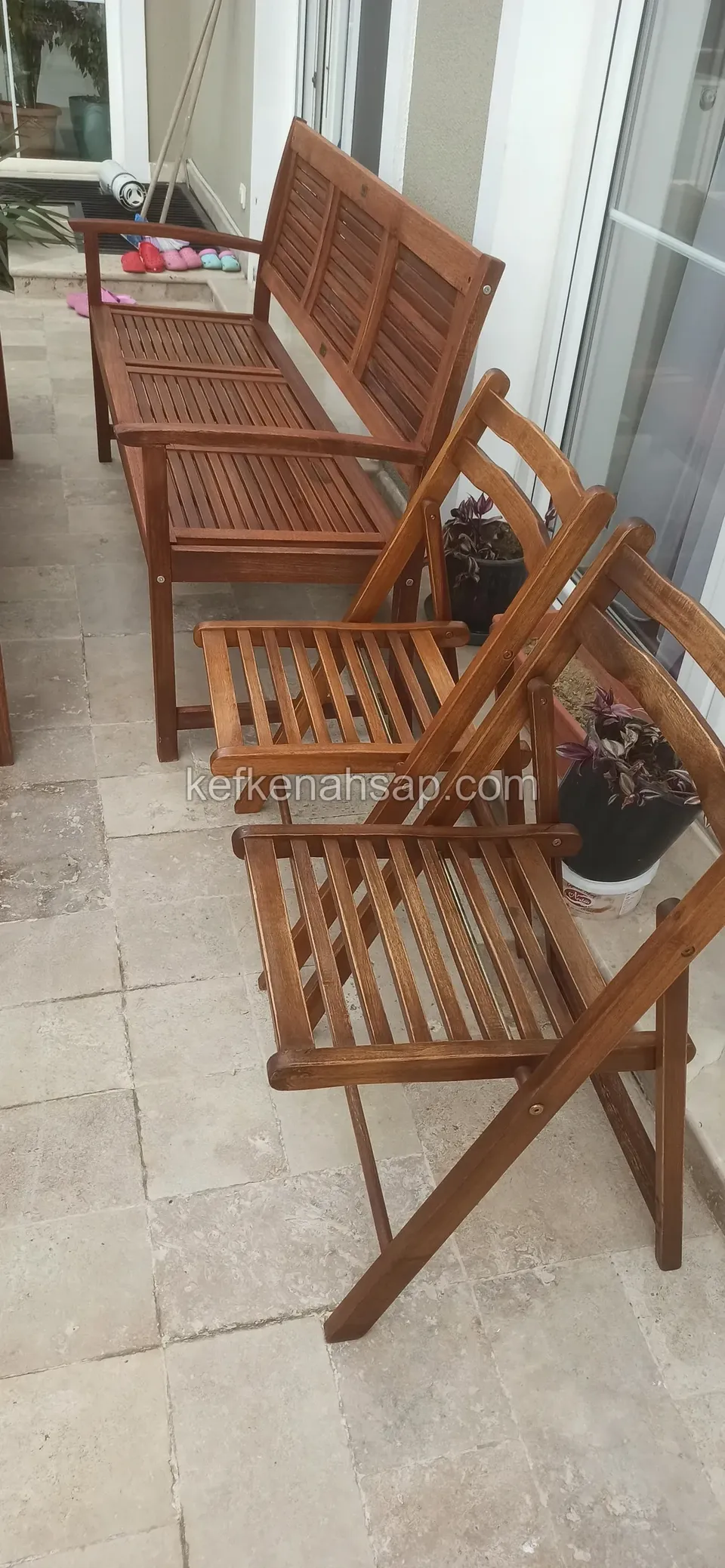 Taş döşemeli dar terasta ahşap kanepe ve yan yana duran iki katlanır sandalye