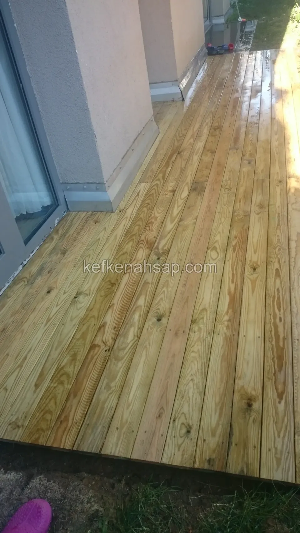 Newly laid light timber deck along a narrow side terrace, gleaming wet
