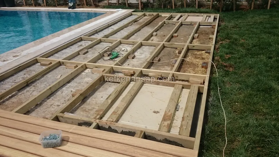 Havuz yanındaki çim alanda, kare gözlere bölünmüş ahşap taşıyıcı çerçeve ve alt kenarda döşenmiş deck tahtaları