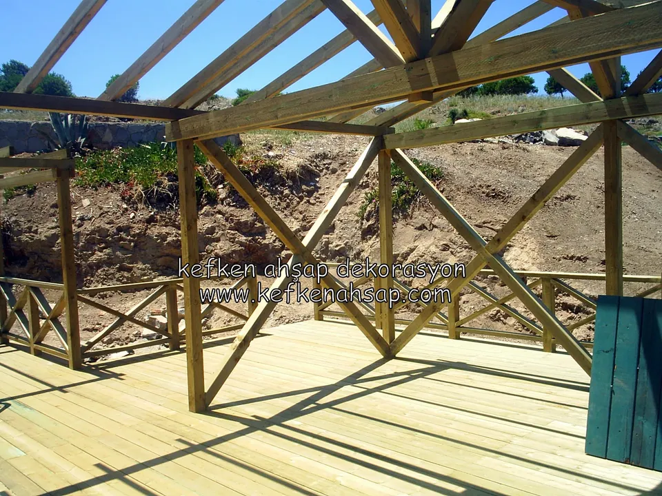 Deck üzerinde çapraz payandalarla güçlendirilmiş pergola iskeleti, arkada kazılmış toprak şev ve alçak korkuluk