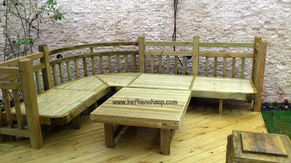 Corner bench with a slatted back and a low table on a timber deck, in front of a stone-clad wall