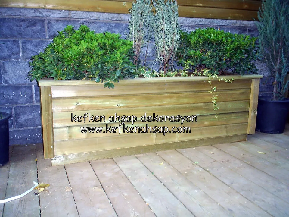 Wide timber planter of horizontal boards with green shrubs standing on a timber deck in front of a stone wall