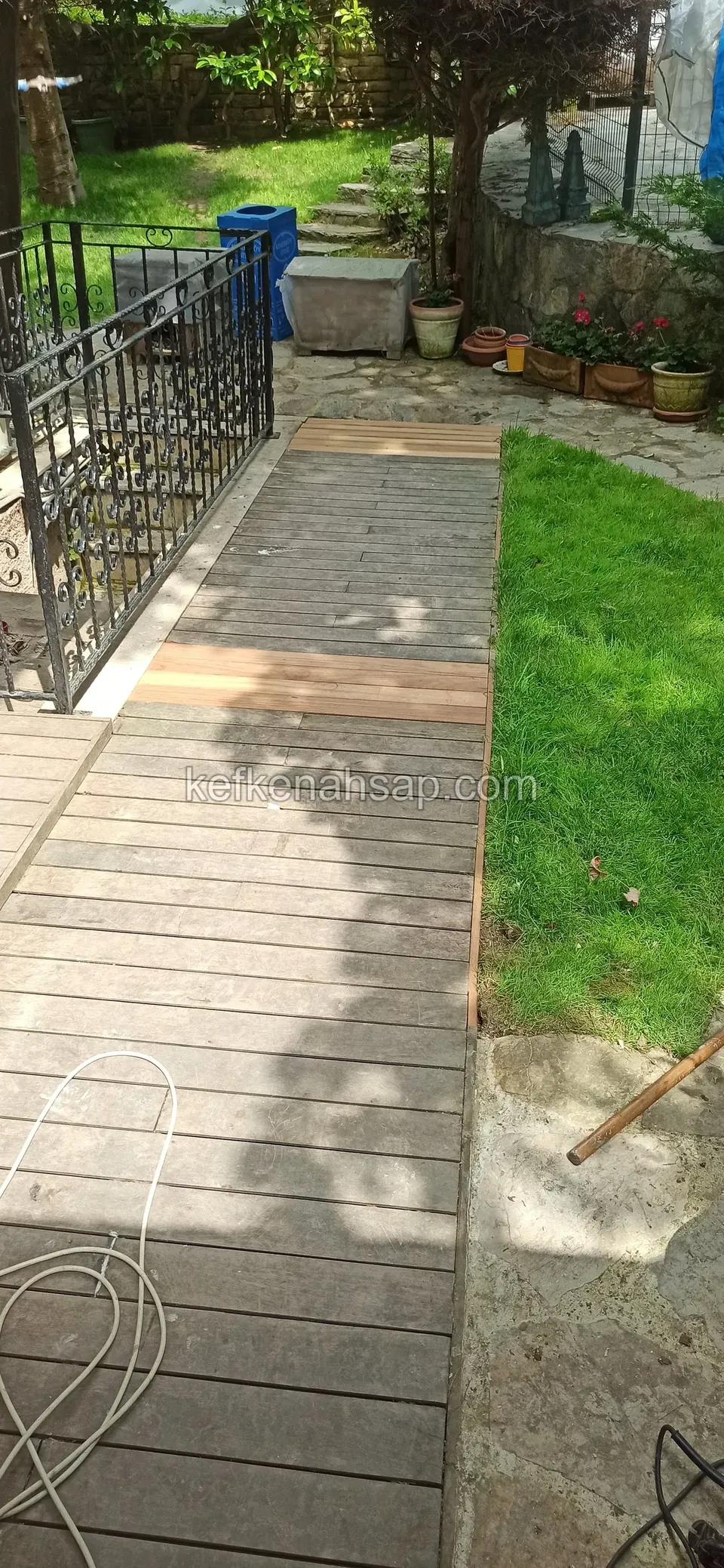 Demir korkuluk yanında bahçeye inen gri eskimiş deck yolu, ucunda yeni açık renkli tahtalar