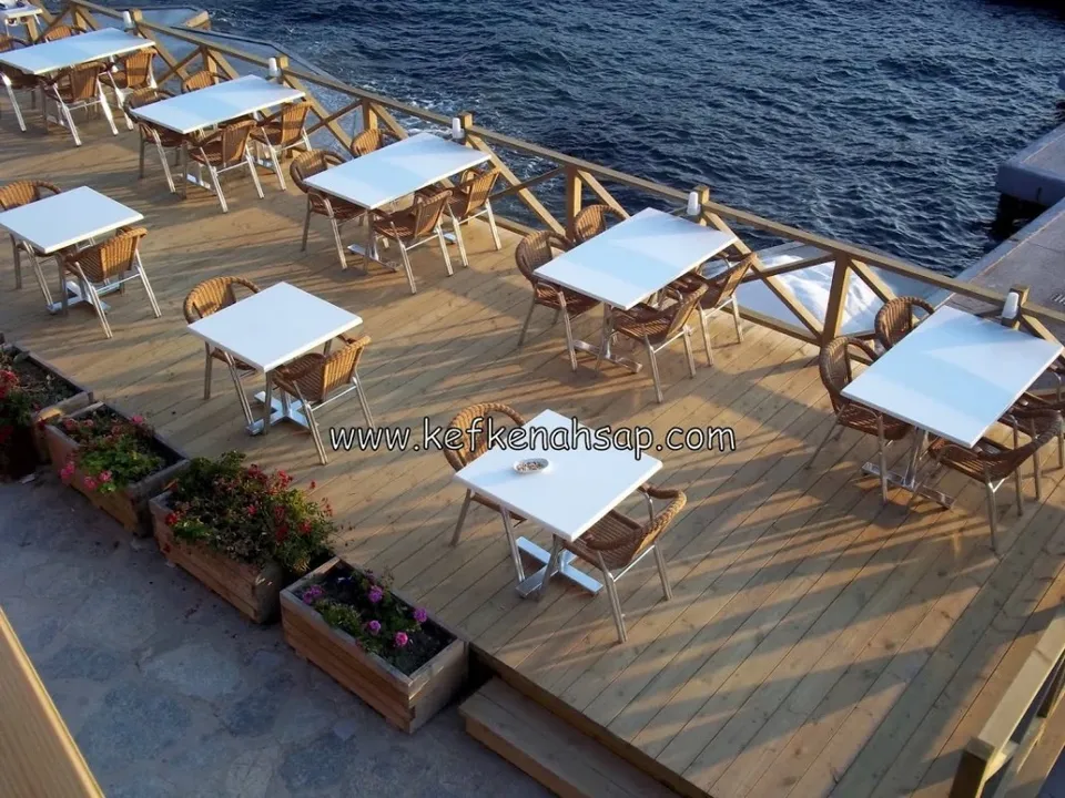 Deniz kıyısında ahşap deck zemin, korkuluklar ve üzerinde oturma grupları olan kafe terası.