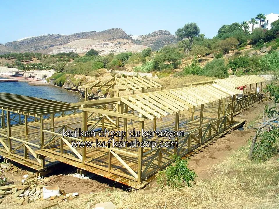Deniz kıyısında ahşap platform üzerine kurulan pergola ve gölgelik karkas iskeleti.