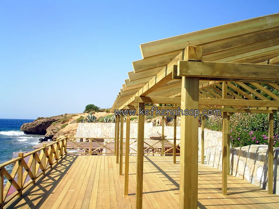 Kayalık kıyıya bakan ahşap deck, çapraz korkuluklar ve deck boyunca uzanan ahşap pergola