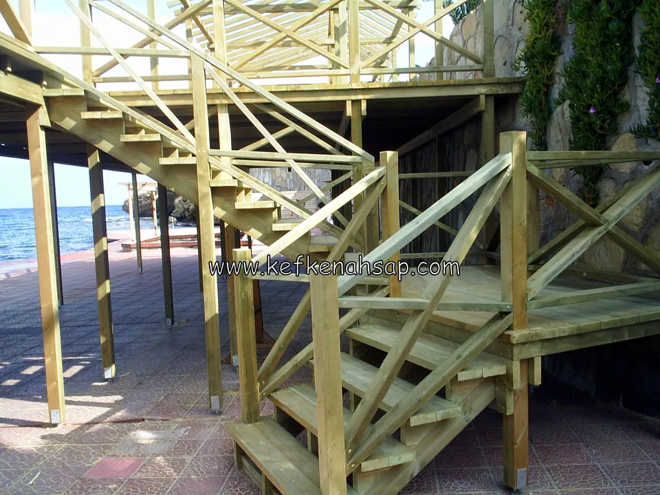 Holztreppe und Kreuzstreben-Geländer auf einer Plattform am Wasser, dahinter das Meer und Holzpfosten