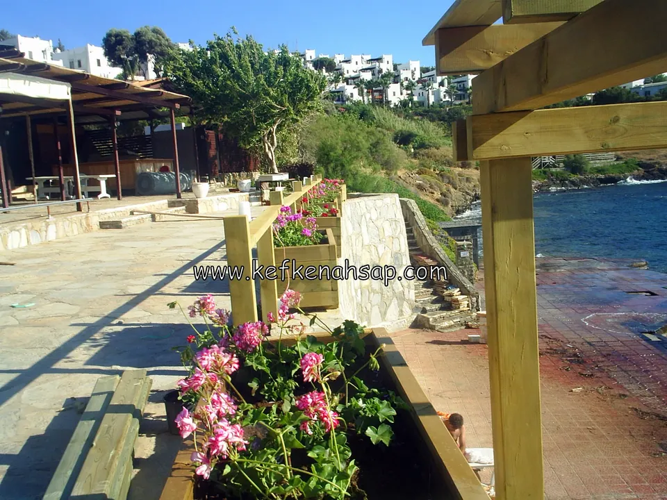Denize bakan taş döşeli teraste ahşap çiçeklik kutusu ve pergola direği, çiçekler pembe