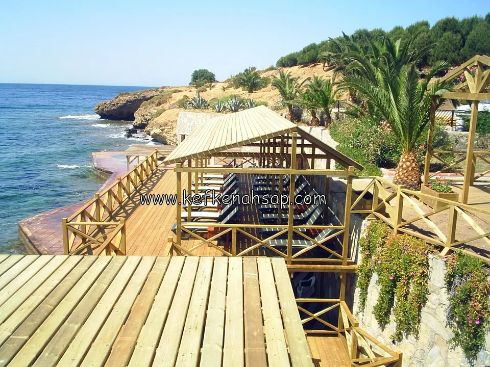 Timber boardwalk along a rocky shore with a slatted timber shade roof over sun loungers