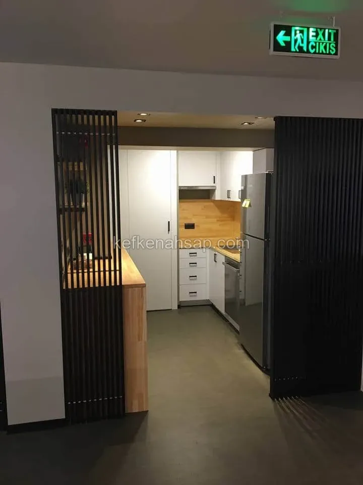 Küche mit weißen Schränken, Holzarbeitsplatte und Edelstahlkühlschrank hinter schwarzen senkrechten Lattenpaneelen