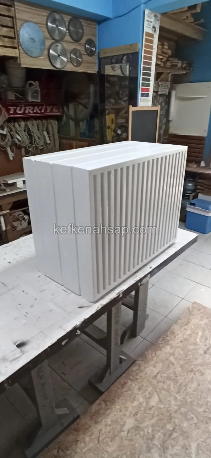 صندوق مطلي بالأبيض بواجهة من قضبان عمودية موضوع على طاولة عمل في الورشة
