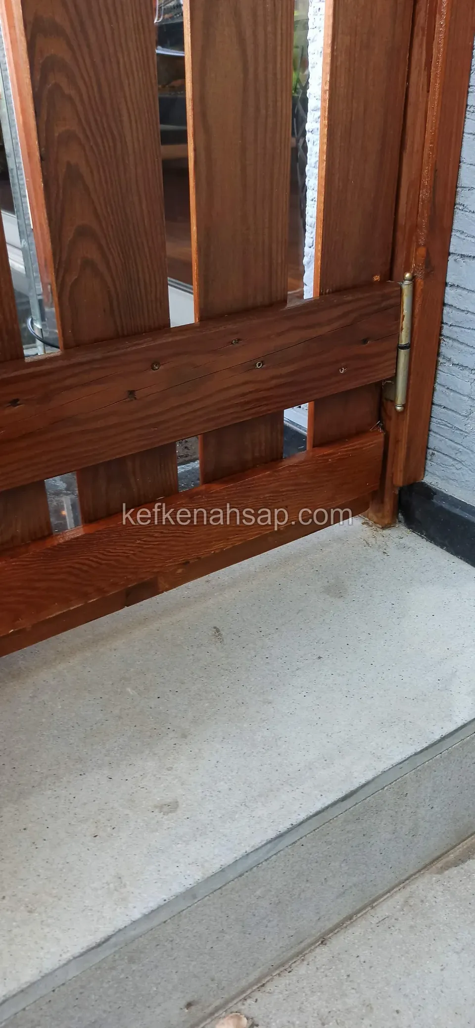 Beton eşik üzerinde duran, dikey tahtalı vernikli ahşap kapı kanadının alt köşesi, yatay kuşak ve menteşe