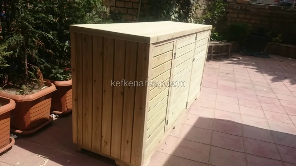 Terasta duran, yan yüzü dikey tahtalı uzun ahşap kasa; önde terakota saksılar, arkada duvar ve bitkiler