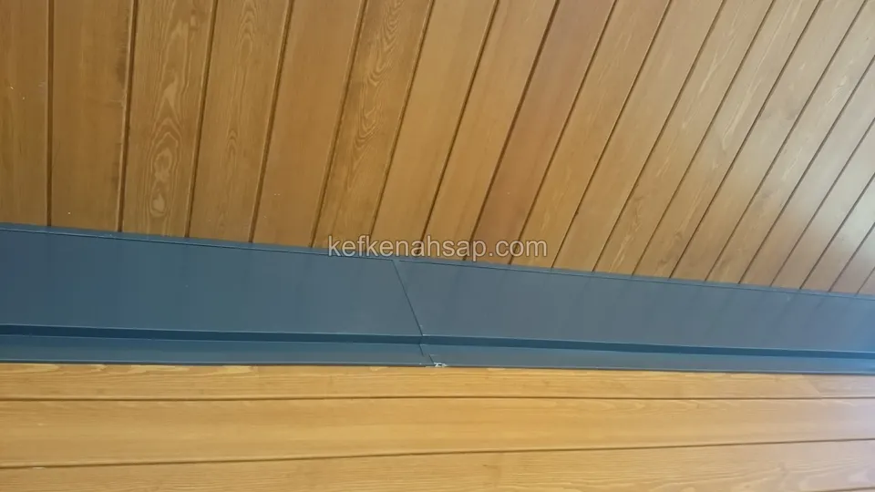 Dikey dizilmiş ahşap tavan tahtaları, altında koyu gri bant ve onun altında yatay cephe tahtaları
