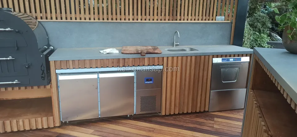 Außenküchenzeile mit Edelstahlkühlschrank und Geschirrspüler zwischen Schränken aus Holzlatten