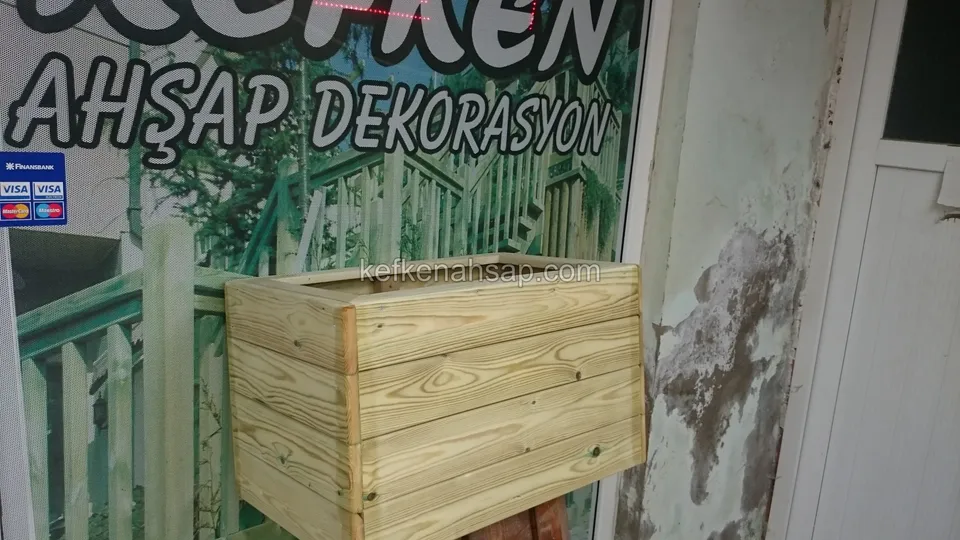 Dükkân duvarının önünde duran, açık renkli yatay tahtalı küçük ahşap çiçeklik