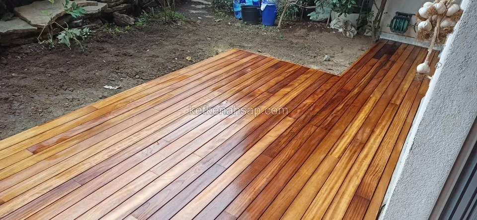 Glossy varnished orange-brown deck along a wall, with soil and plants behind